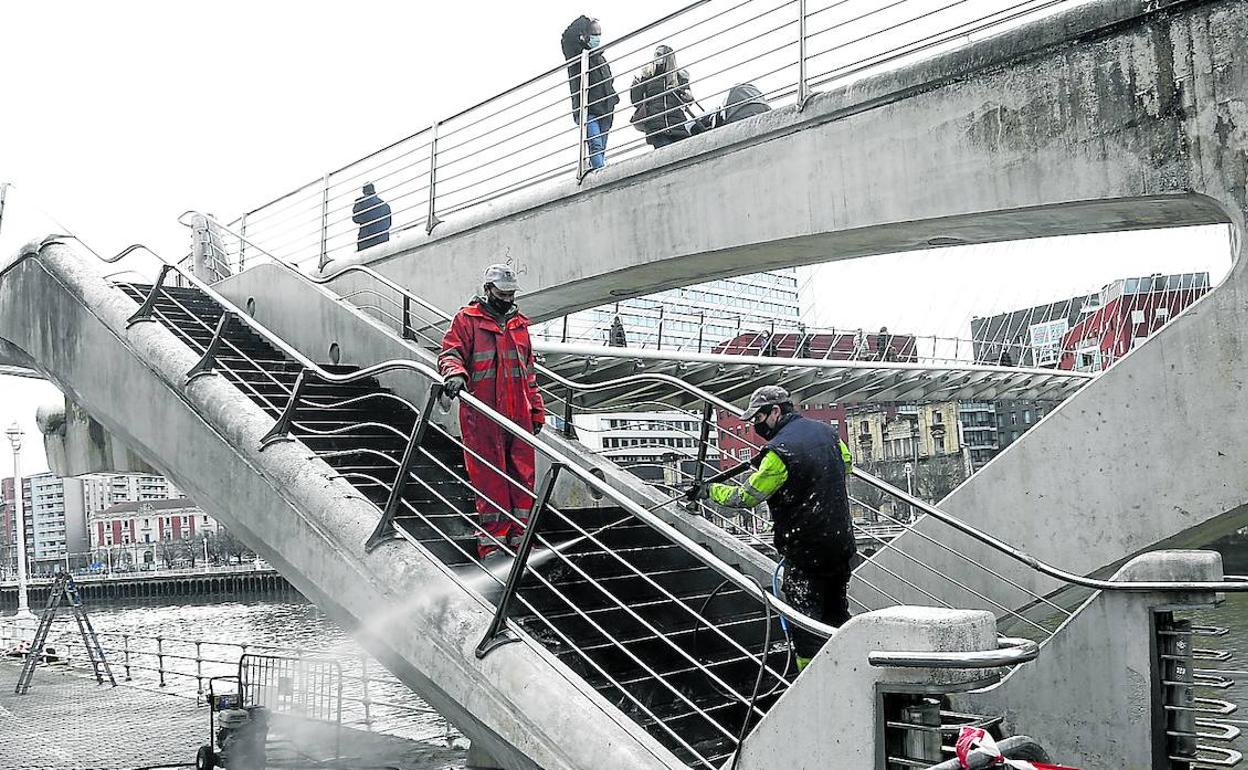 Un operario limpia la escalera en el estribo del lado de Campo Volantín de la pasarela Zubizuri.