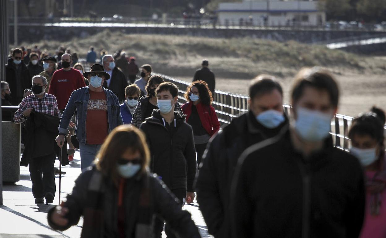 Ciudadanos protegidos con mascarillas pasean frente a la playa de Gorliz. 