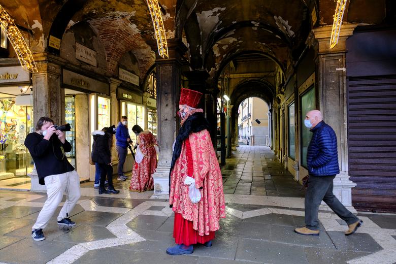 Un fotógrafo toma una foto de una persona vestida con un disfraz de carnaval en la Plaza de San Marcos.