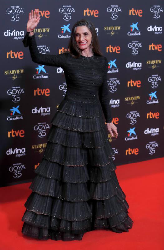 La actriz madrileña recibe este año el Goya de Honor en reconocimiento a toda su carrera. Ha posado en el ‘photocall’ con un bonito diseño de Armani Privé, en el que destaca una falda de vuelo con volantes. Lleva zapatos de Manolo Blahnik y joyas de Bárcena.