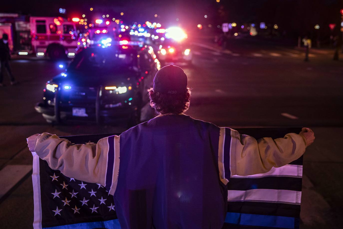 Un transeúnte sostiene una bandera de Thin Blue Line mientras una procesión con el cuerpo de un oficial de policía sale de la tienda de King Sooper.