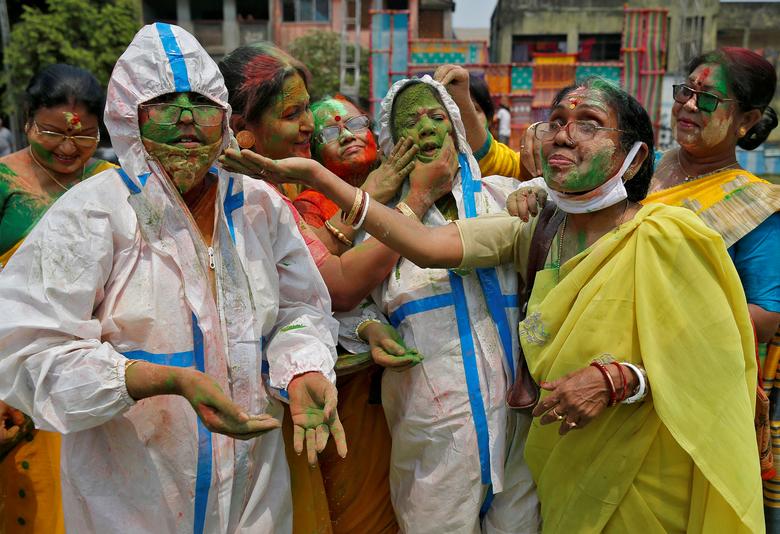 Las mujeres que usan trajes protectores reaccionan cuando se les aplica polvo de color en la cara durante las celebraciones de Holi en Calcuta, India.