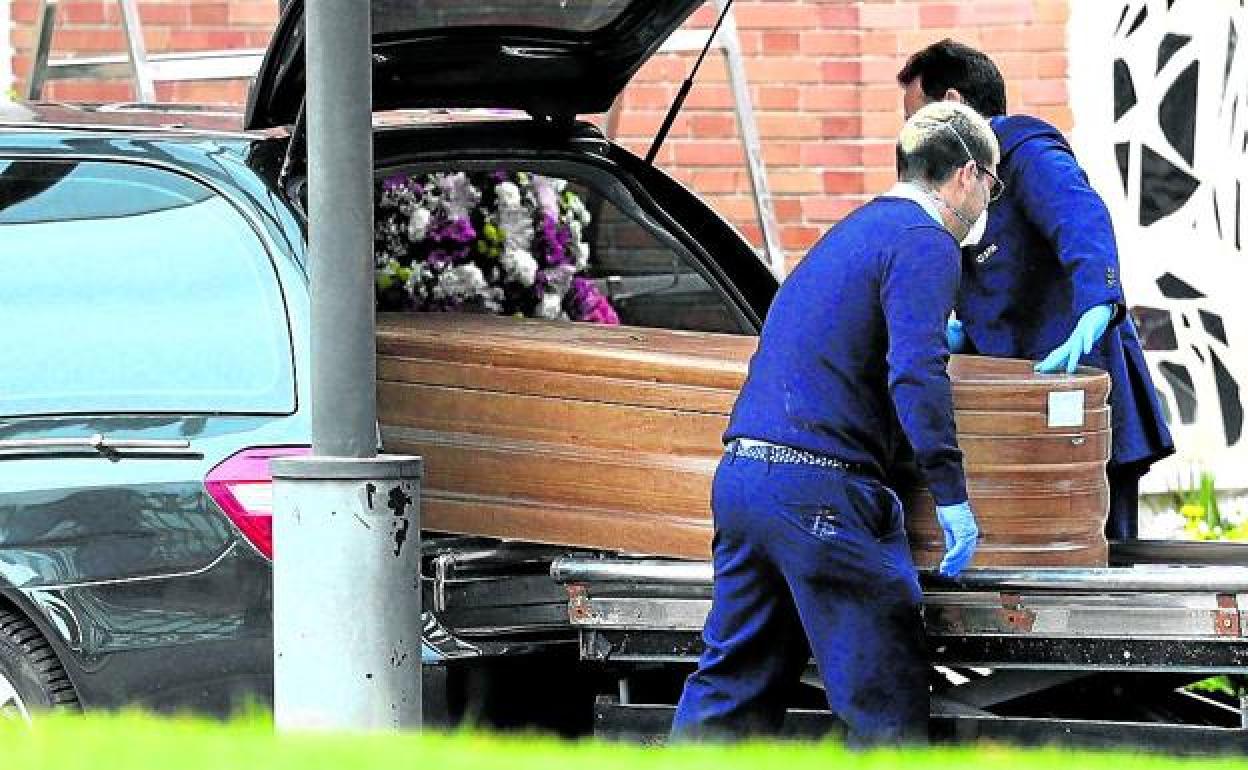 Empleados de una funeraria introducen un féretro en un coche fúnebre. 