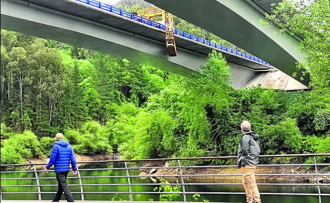 Dos hombres observan cómo los operarios reparan la tubería con una plataforma elevadora. 