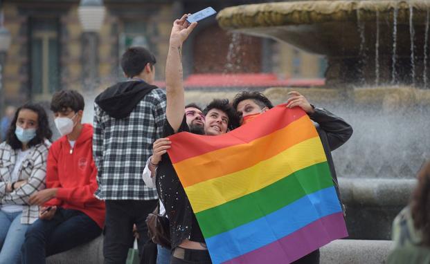 Tres jóvenes se fotografían con la bandera arcoirís durante la manifestación de este lunes en Bilbao.