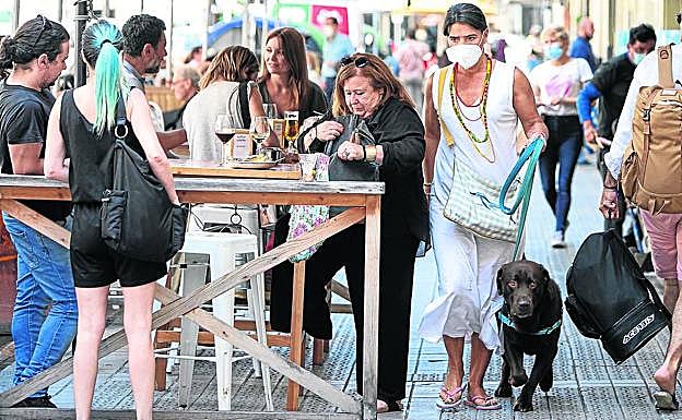Una mujer con su perro pasa por una calle donde los veladores dejan poco espacio a los viandantes. 
