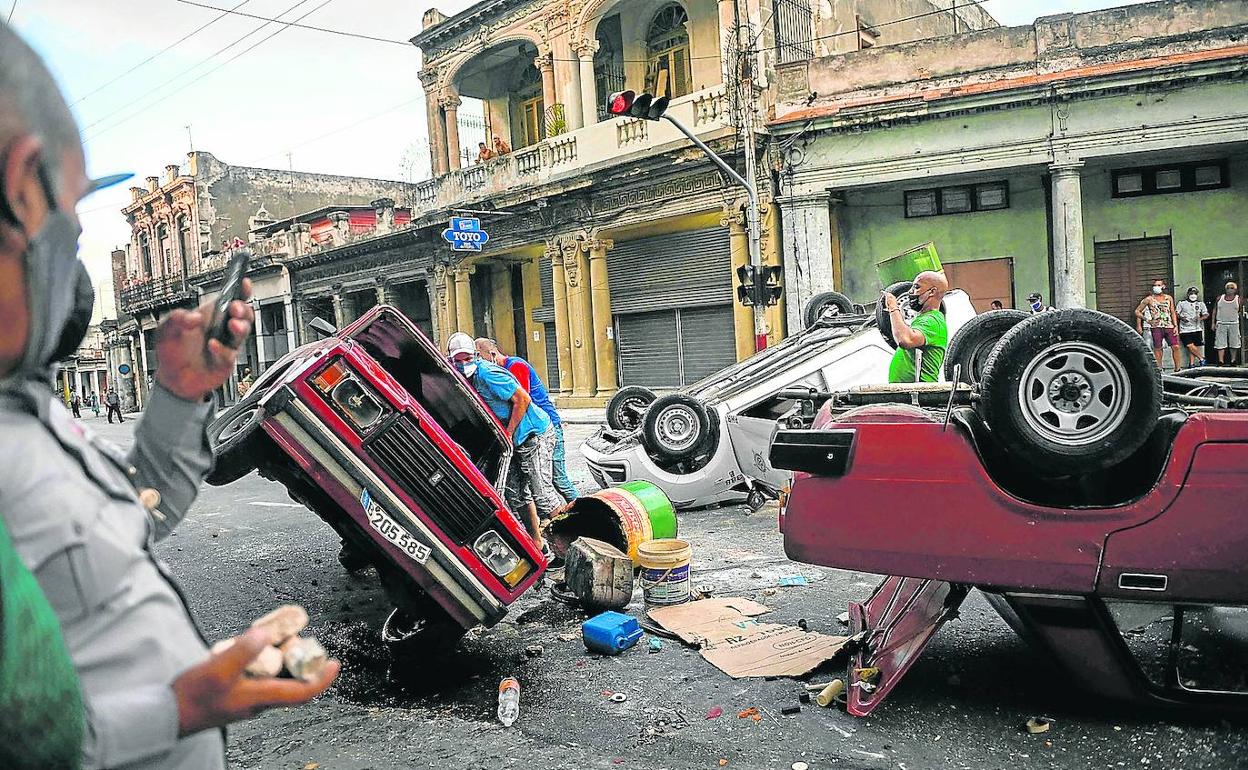 Varias personas intentan recuperar patrullas policiales volcadas en La Habana durante las protestas. 