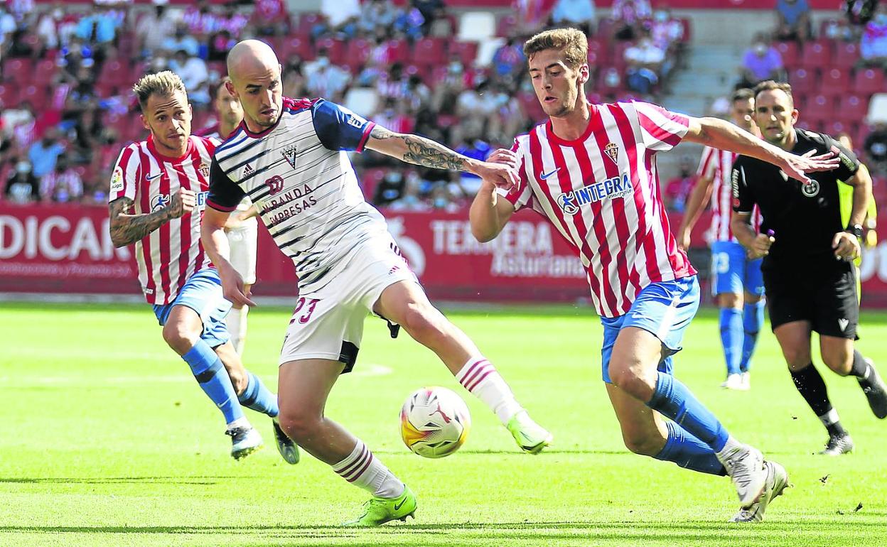 El centrocampista Oriol Rey intenta controlar la pelota ante la presión de dos jugadores del Sporting de Gijón. 