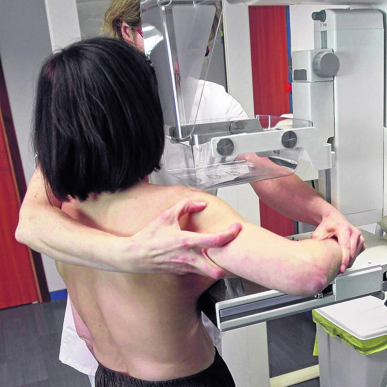 Una paciente se prepara para ser sometida a una mamografía con la ayuda de una sanitaria. 