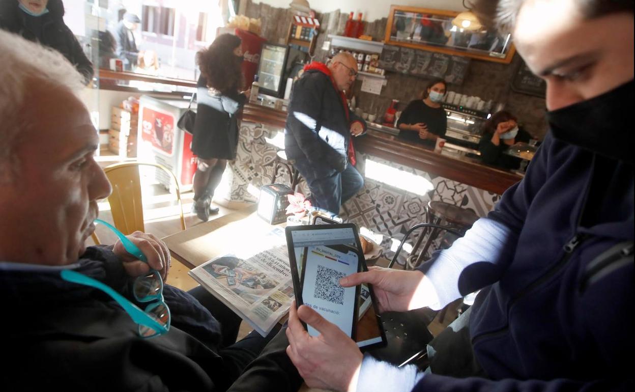 Un par de clientes de un bar de Barcelona consultan el pasaporte covid de uno de ellos. 