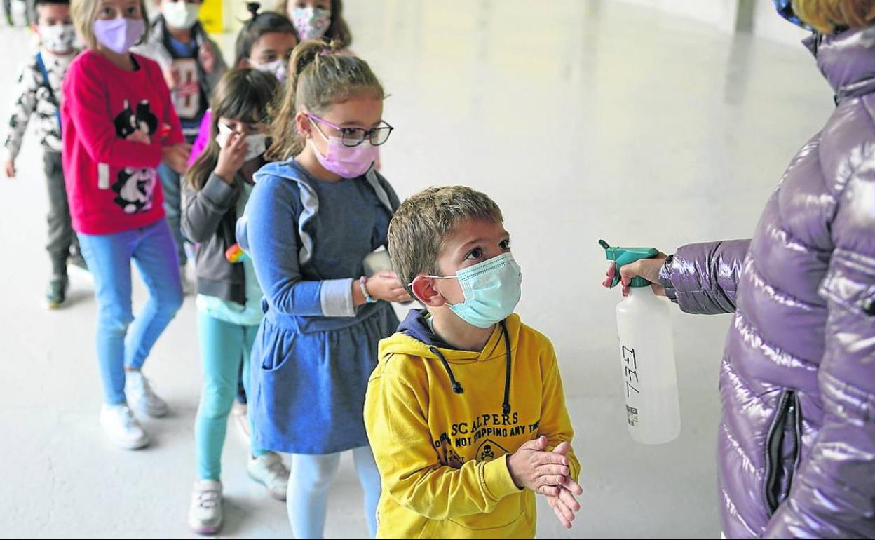 Una profesora rocía las manos de los niños con hidrogel antes de que entren en clase. 