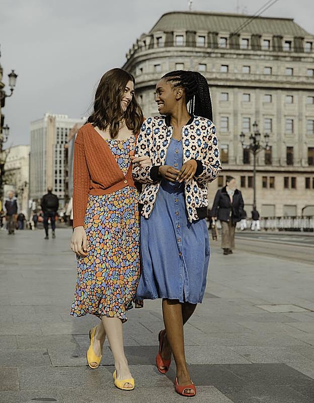 La modelo de la izquierda luce mono de tirantes con rebeca naranja y la joven de la derecha lleva una 'bomber' de verano con vestido denim.