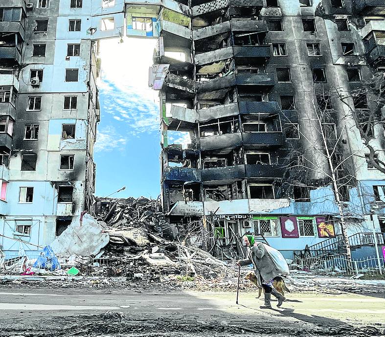 Una anciana pasa delante de un edificio bombardeado.