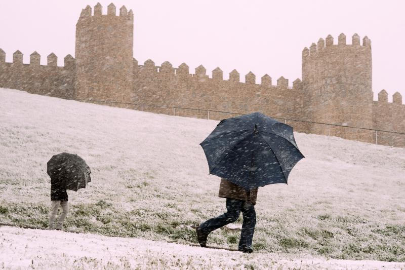 Dos personas se protegen de la nieve junto a la muralla de Ávila este miércoles. 