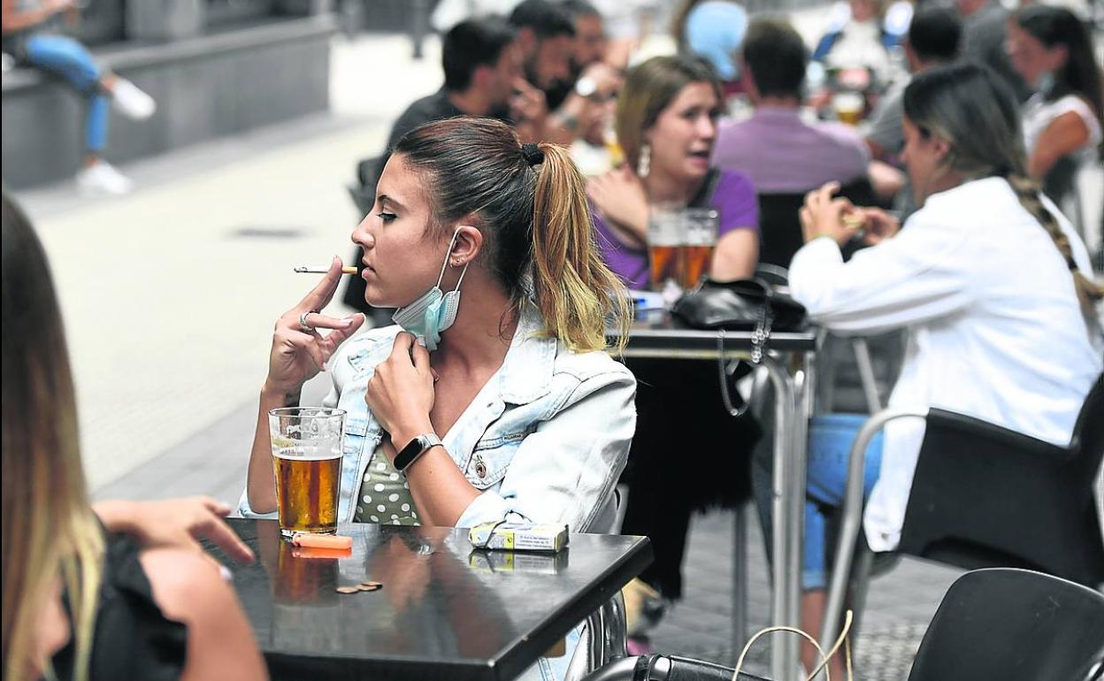 Una joven se fuma un cigarrillo, mientras consume una cerveza en la terrraza de un bar. 