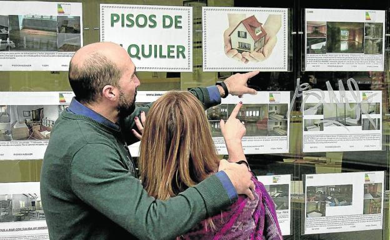 Una pareja consulta anuncios de viviendas en alquiler de una inmobiliaria.