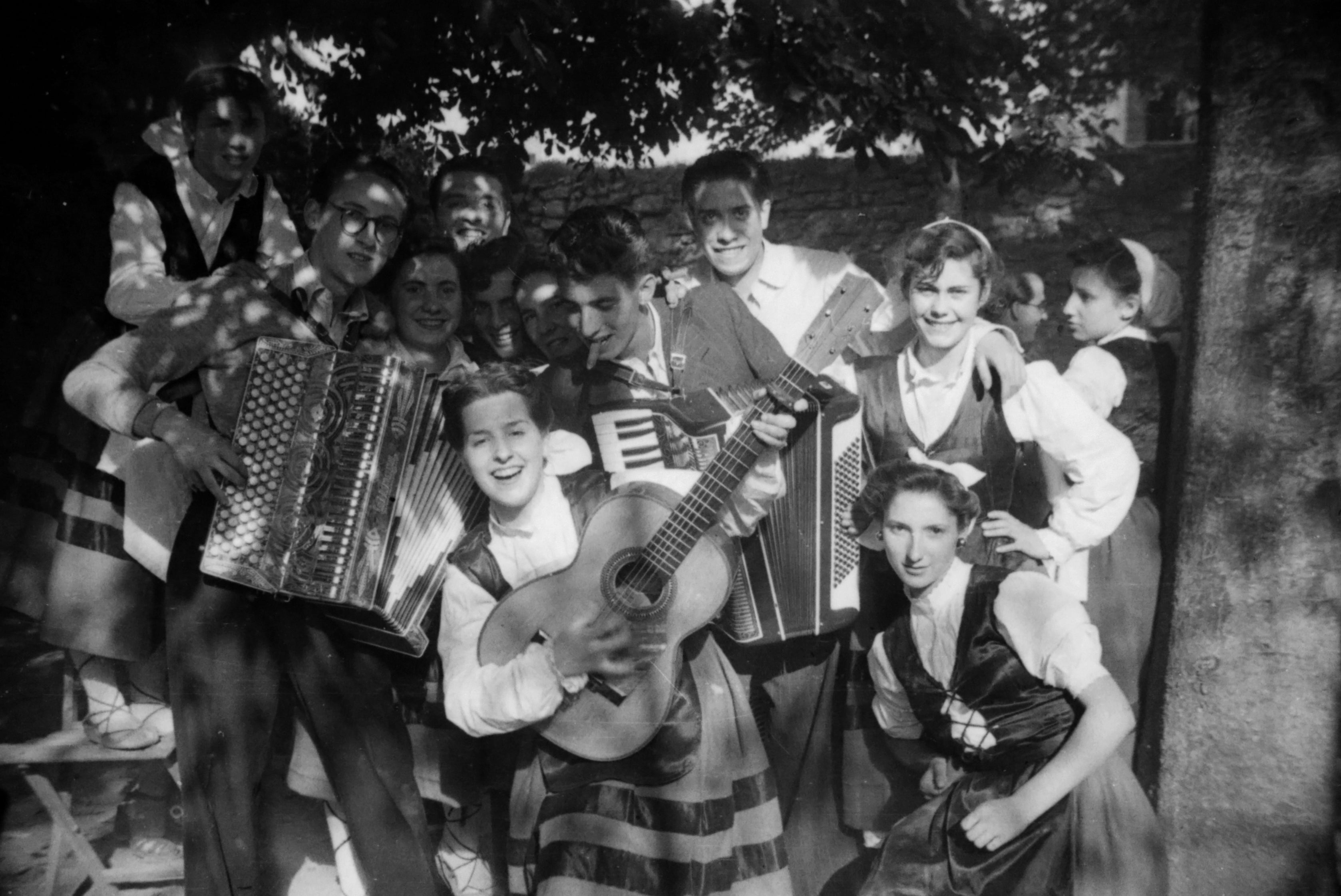 Retrato en exterior de un grupo de mujeres jóvenes vestidas con trajes regionales alaveses que posan acompañadas de músicos durante la celebración de una fiesta en Alegría