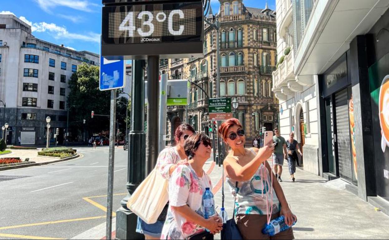 Tres mujeres se hacen un selfie junto a un térmometro de Moyua que este mediodía marcaba 43º.
