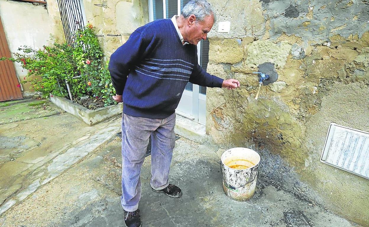 Un vecino carga un caldero de agua con un grifo colocado en el exterior de su vivienda. 