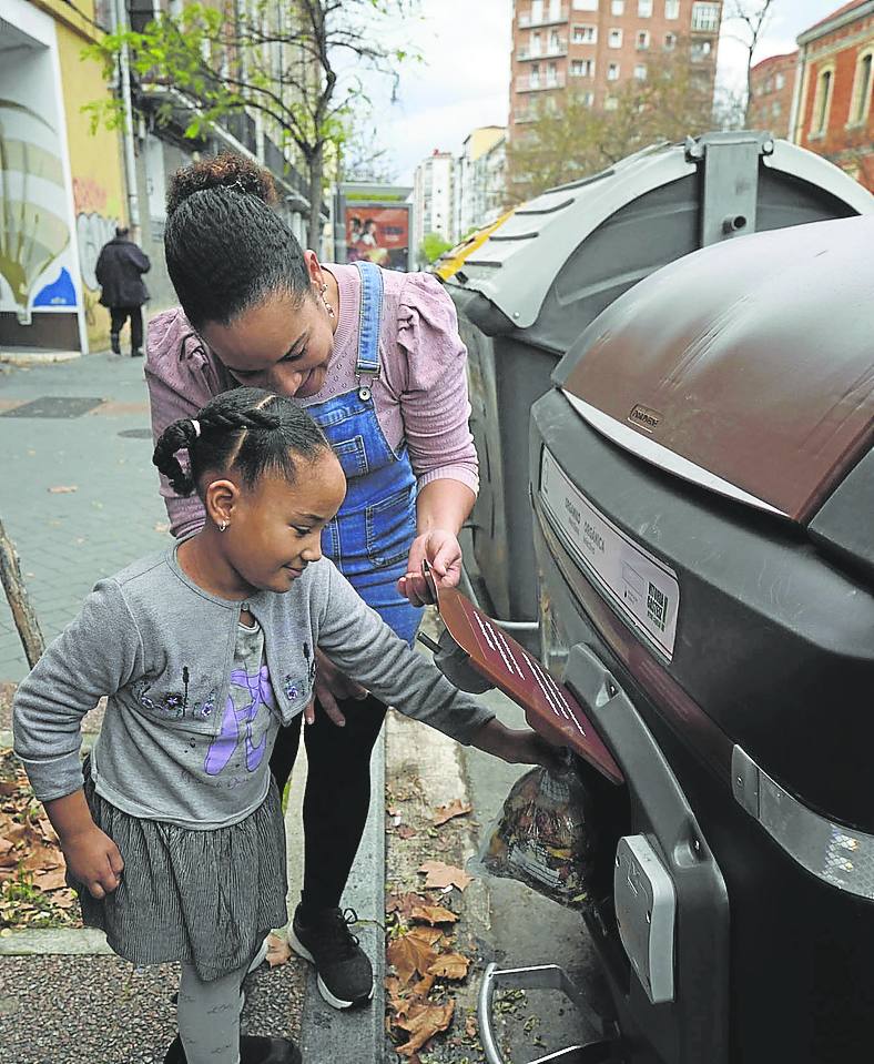 Una madre enseña a su hija a utilizar el contenedor con 'chip' en el barrio de San Cristóbal