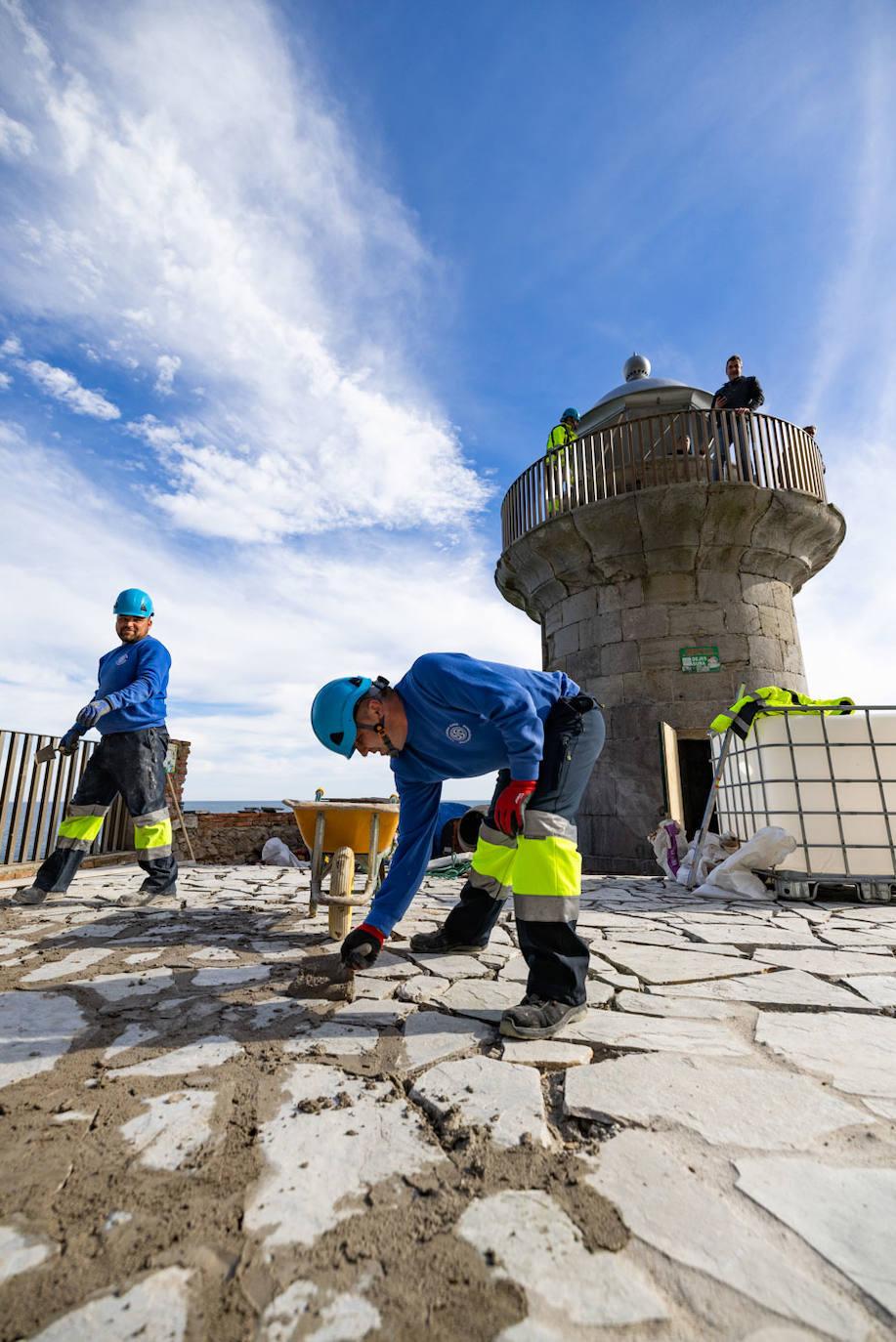 Dos operarios trabajan en la mejora del firme del área del faro con el alcalde, Sergio Abascal, observándoles desde la torre.