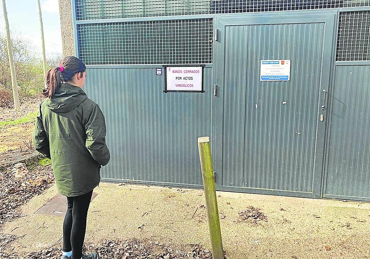 Una joven lee el letrero de 'Cerrado por actos vandálicos', en la puerta de los aseos, ayer por la mañana.