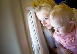 Un bebé ajeno a esta información mira por la ventana de un avión, mientras viaja en el regazo de su madre.