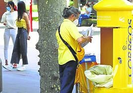 Una cartera recoge las cartas de un buzón ubicado en calle La Estación.