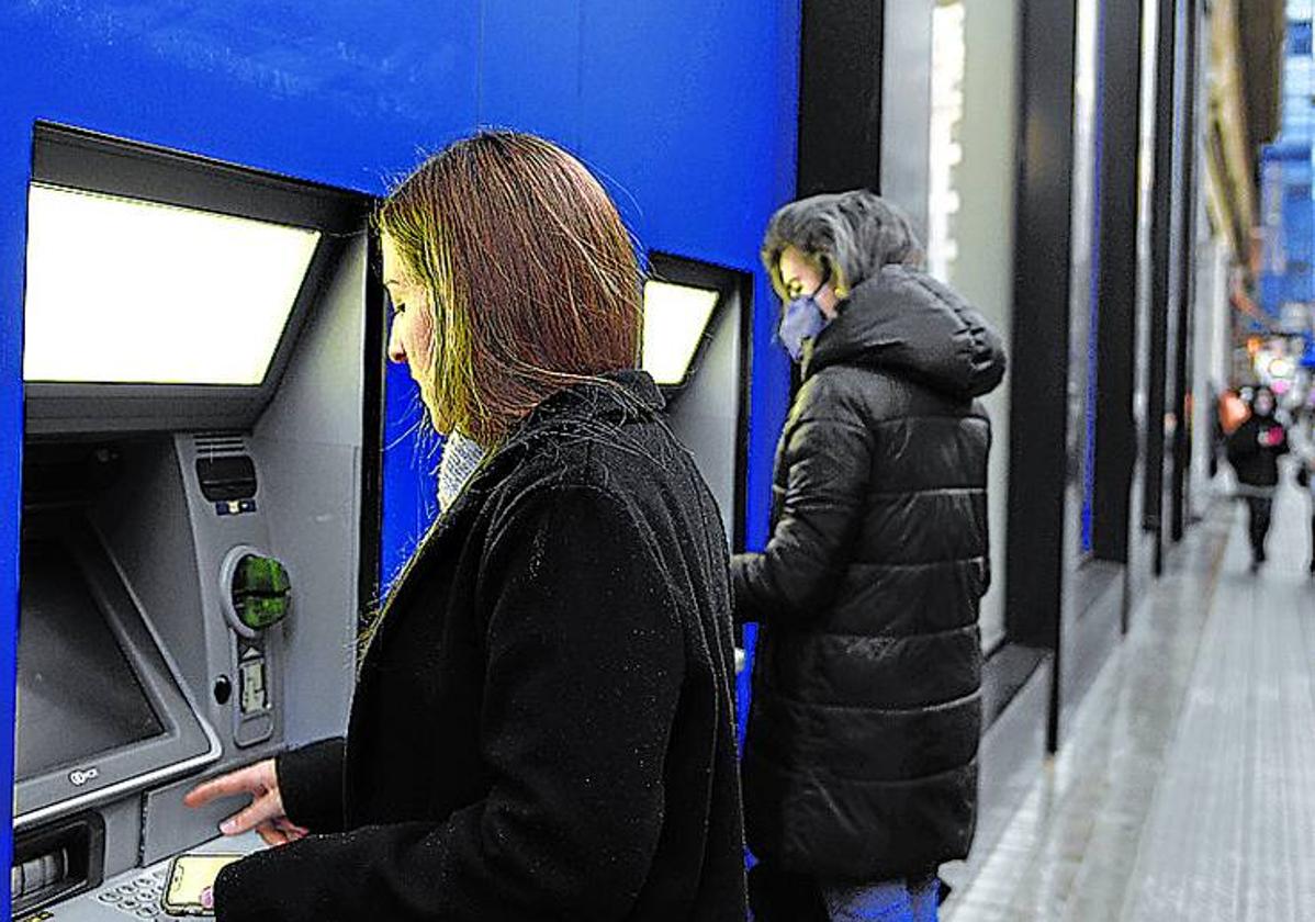 Dos mujeres sacan dinero en cajeros automáticos.