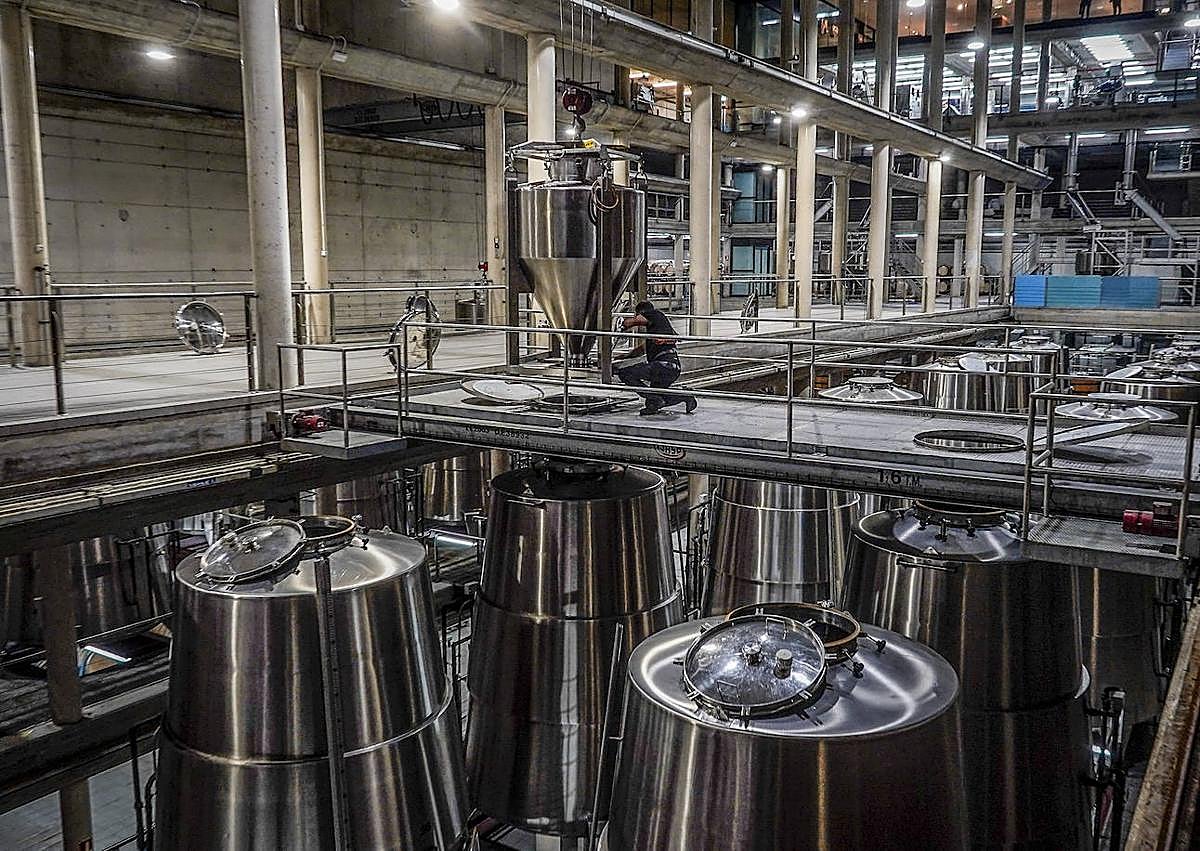 Imagen secundaria 1 - Arriba, Laura, química, toma muestras de las uvas que llegan en las cajas a la recepción. Debajo, la bodega, con los depósitos de forma de cono truncado de refulgente acero. El espacio, de puro hormigón, recuerda a un hangar de sondas espaciales. 