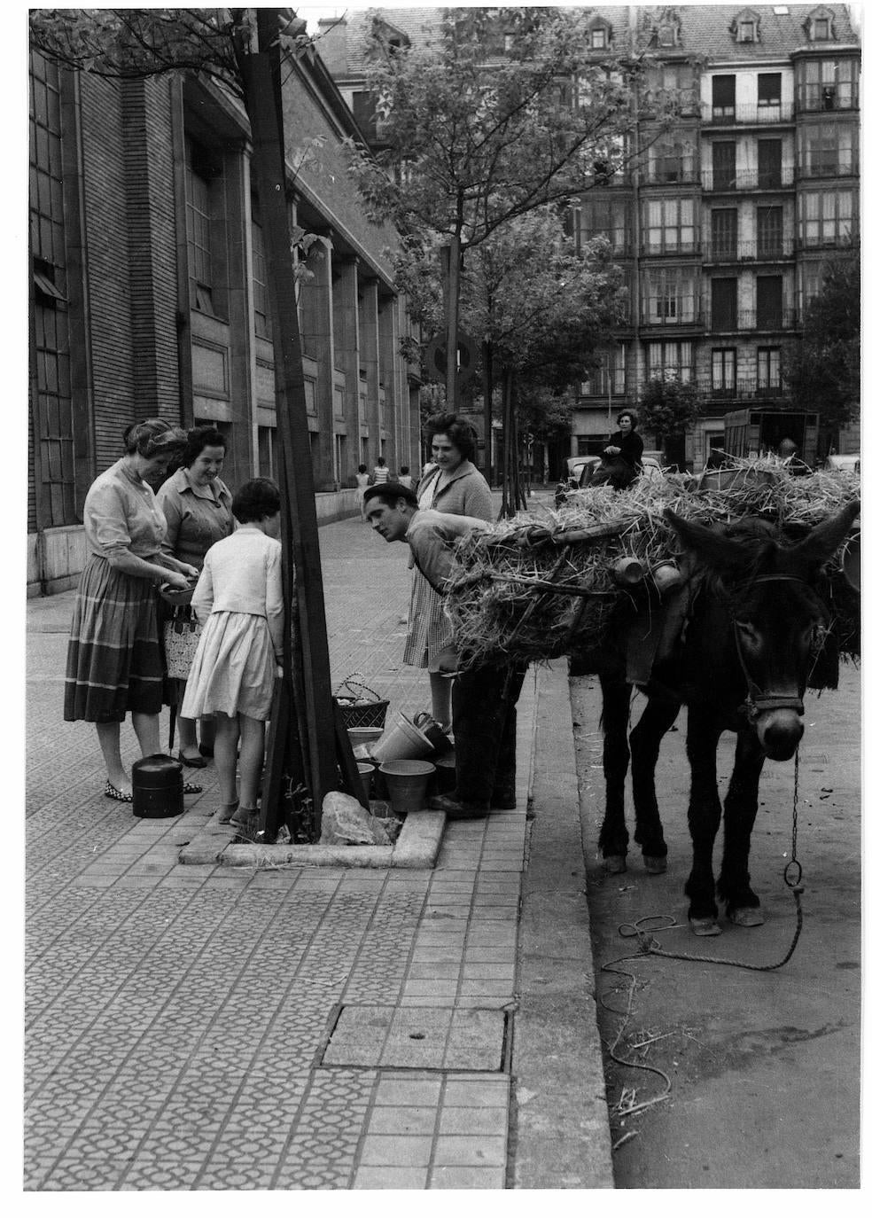 No solo vendían botijos, pero la castiza vasija con asa y pitorro servía para dar nombre a estos ambulantes de la alfarería, que aparejaban sus borricos con unas angarillas de ramas de encina donde transportaban su tesoro de barro. En la imagen, un botijero atiende a unas clientas junto al mercado del Ensanche.