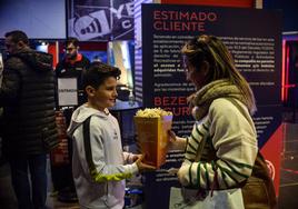 Una madre y su hijo pasan con un paquete de palomitas frente al cartel que prohíbe introducir comida de fuera en los cines Yelmo de Megapark.