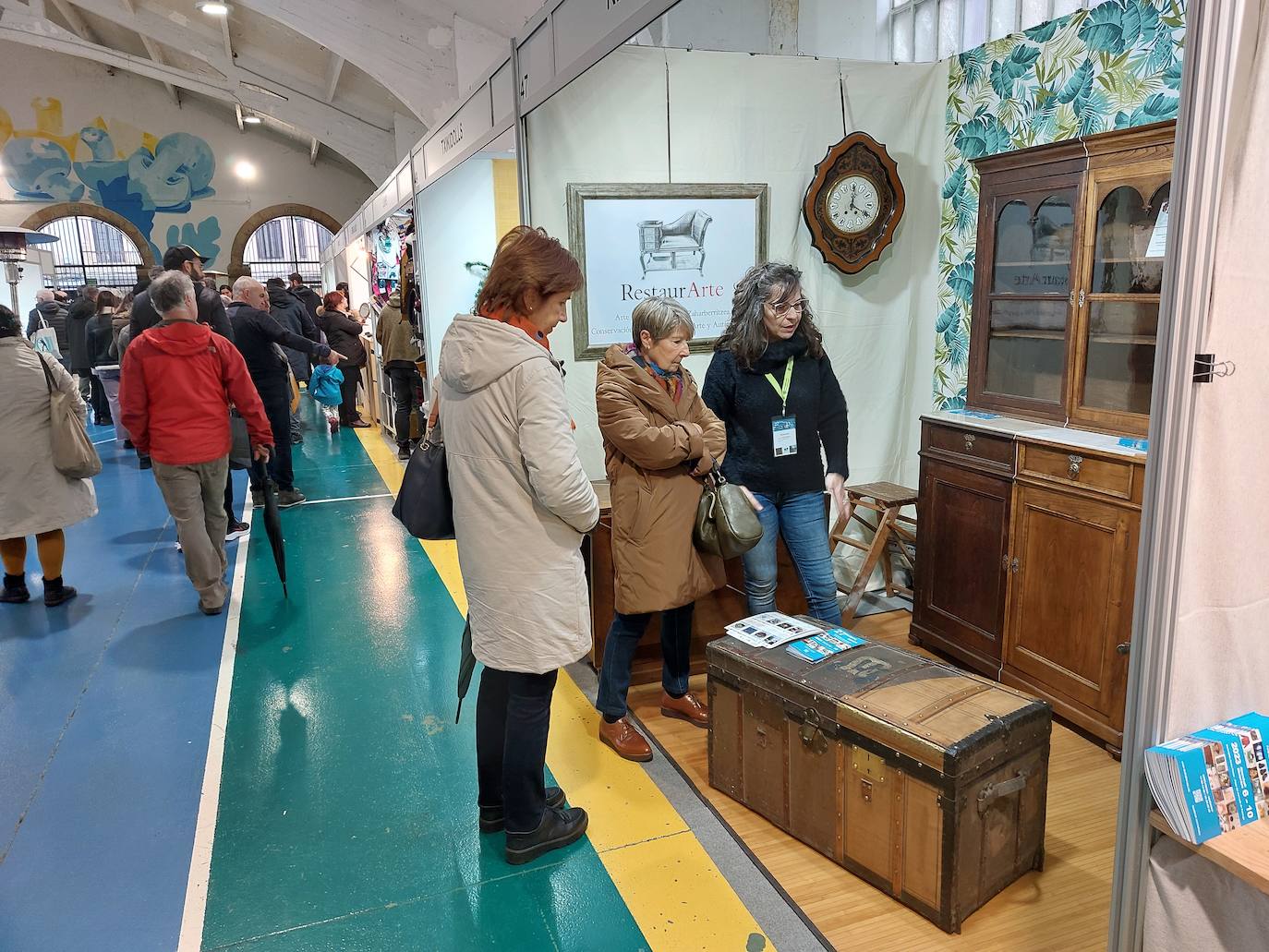 Dos de las asistentes muestran su interés por unos muebles artesanales de la empresa duranguesa RestaurArte en la Plaza del Mercado