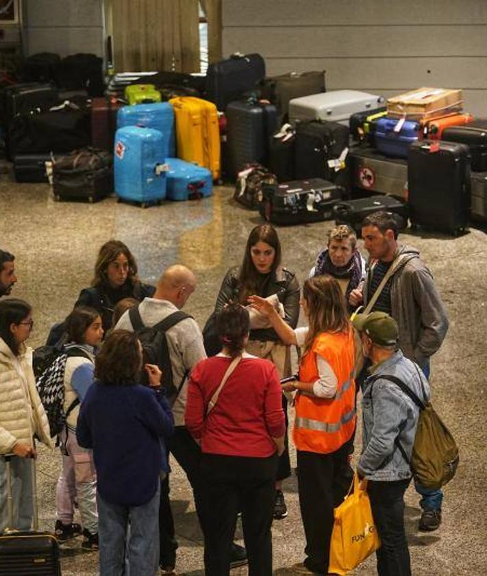 Imagen secundaria 2 - Arriba, largas colas en el 'hall' de salidas de Loiu. A la izquierda, empleados de una empresa de transporte cargan en furgonetas las maletas que se han quedado en tierra. A la derecha, usuarios reciben información de parte de una trabajadora con las cintas transportadoras colapsadas.