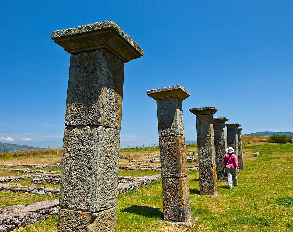 Una mujer camina junto a los restos del porticado del Decumanus de Julióbriga.