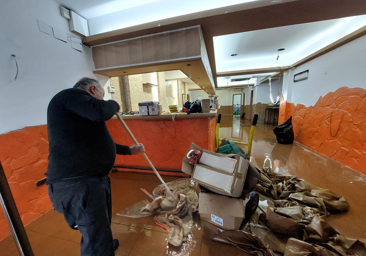 El propietario de un bar de la calle Obieta recoge el agua que dejó el episodio de crecida del lunes.