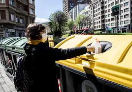 Una mujer deposita un envase de plástico en un contenedor amarillo.