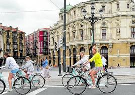 Turistas foráneos circulan en bicicleta por las inmediaciones del teatro Arriaga de Bilbao.