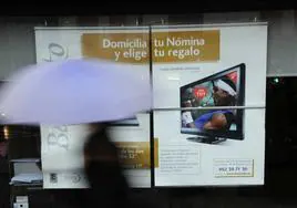 Una persona pasa por delante de un cartel promocional de un banco.