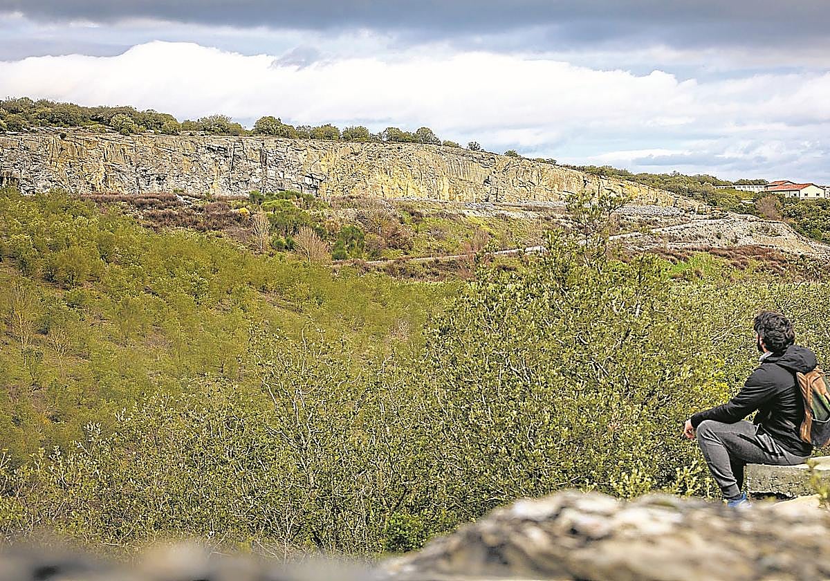 Un joven sentado observa el paisaje con la mina de Nanclares en el horizonte.