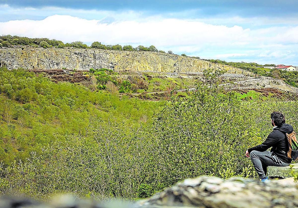 Un joven sentado observa el paisaje con la mina de Nanclares en el horizonte.
