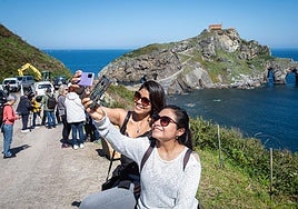 Dos visitantes se fotografían con el islote de Gaztelugatxe de fondo.
