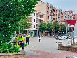 Dos operarios de jardinería en la plaza de la estación del metro de Algorta con un coche patrulla de la Ertzaintza a escasos metros.