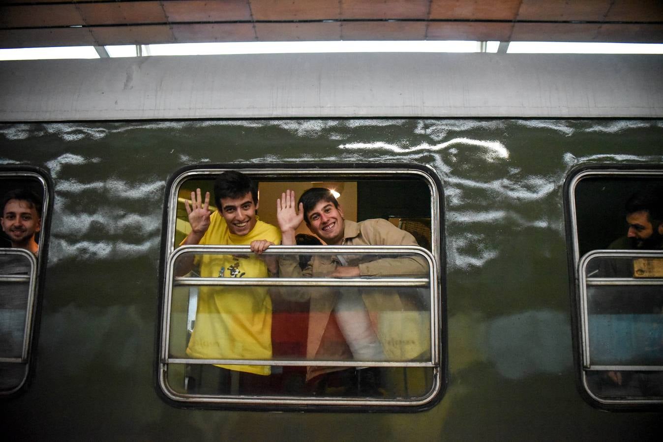 Dos viajeros saludan desde la ventanilla al llegar.