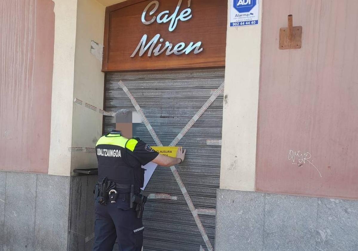 Un agente de la Policía Local colocando el precinto en la puerta de entrada al bar.