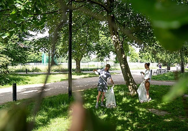 Dos personas recogiendo basura en un parque.