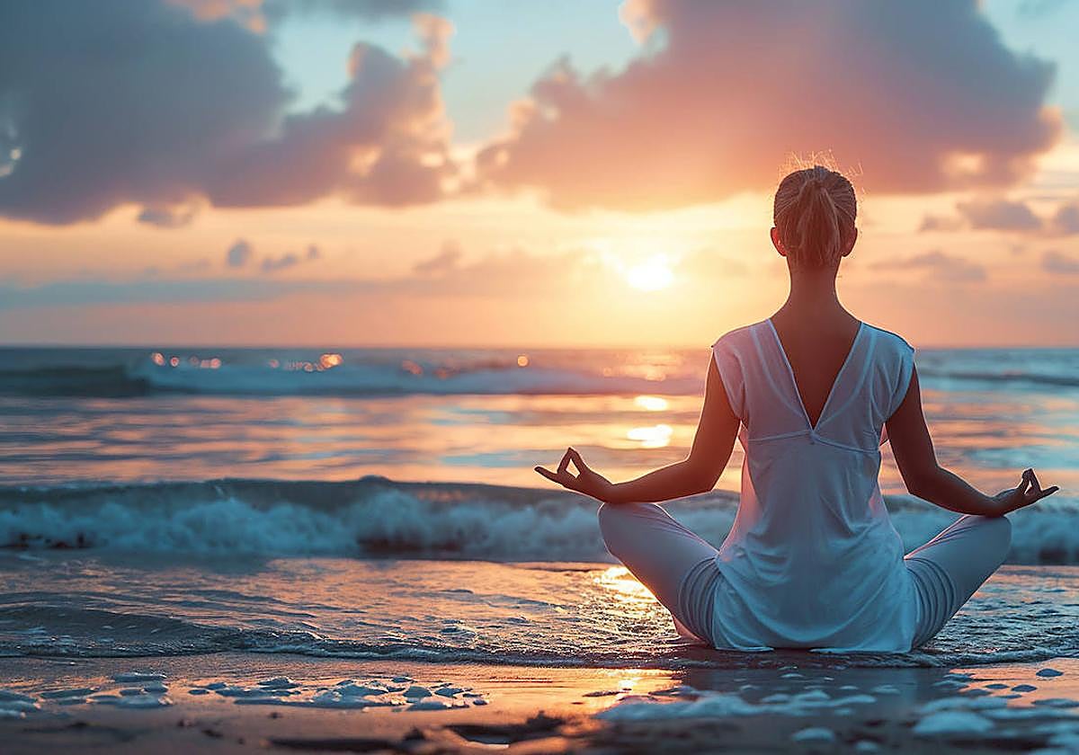 Una mujer practica la meditación en una playa, al atardecer a la orilla del mar.