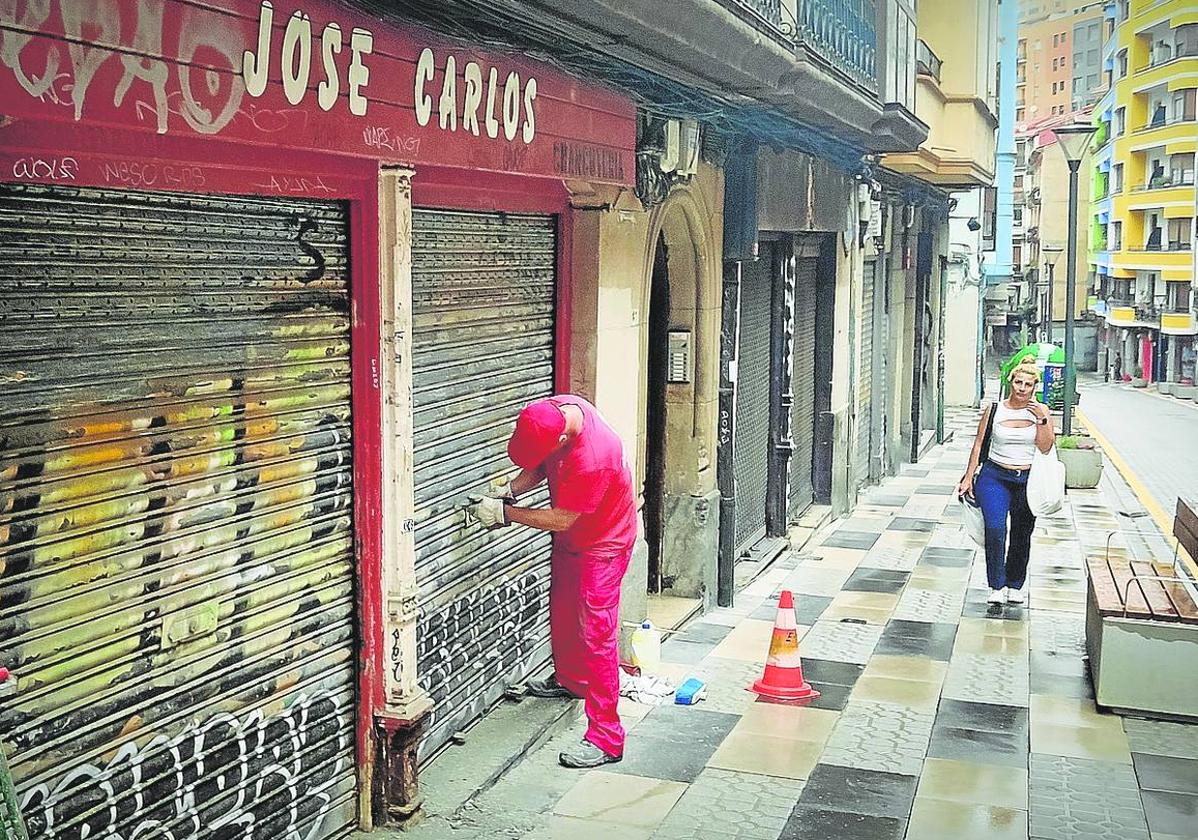 Operarios municipales raspaban ayer las pintadas que afean muchas lonjas de la calle.