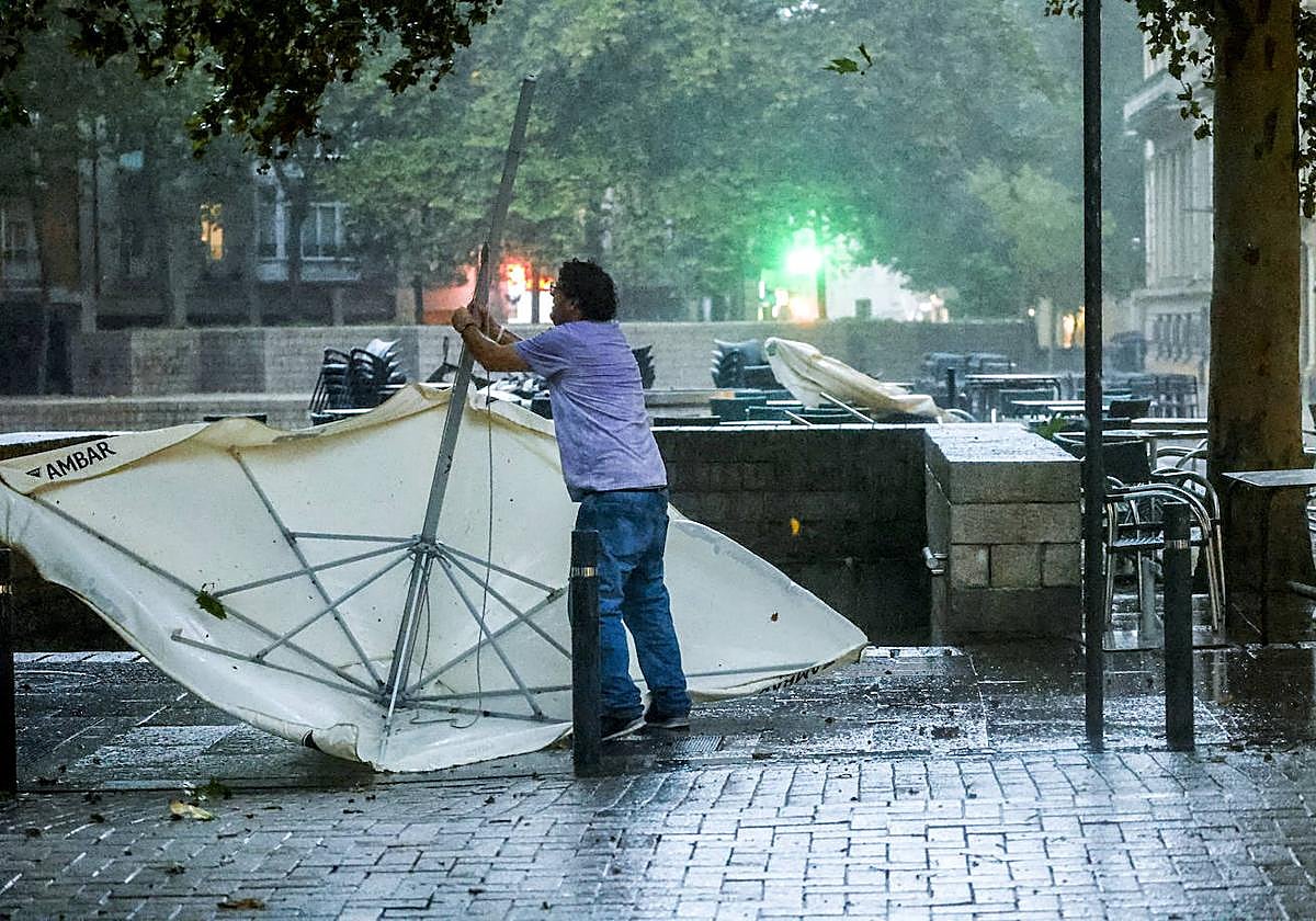 Un hostelero retira una sombrilla arrastrada por el viento en mitad del chaparrón.