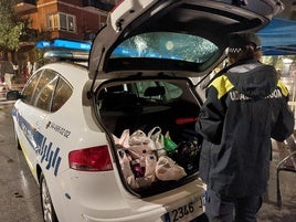 Una agente transporta al vehículo policial las botellas que han sido decomisadas